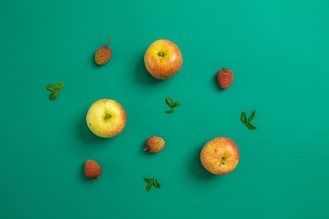 A flat lay of apples, strawberries and leaves against a turquoise backdrop