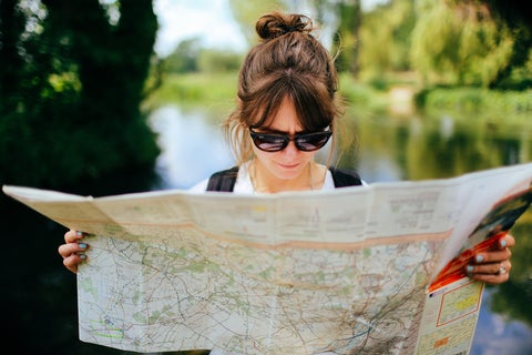 A woman wear sunglasses staring down at a big, paper map
