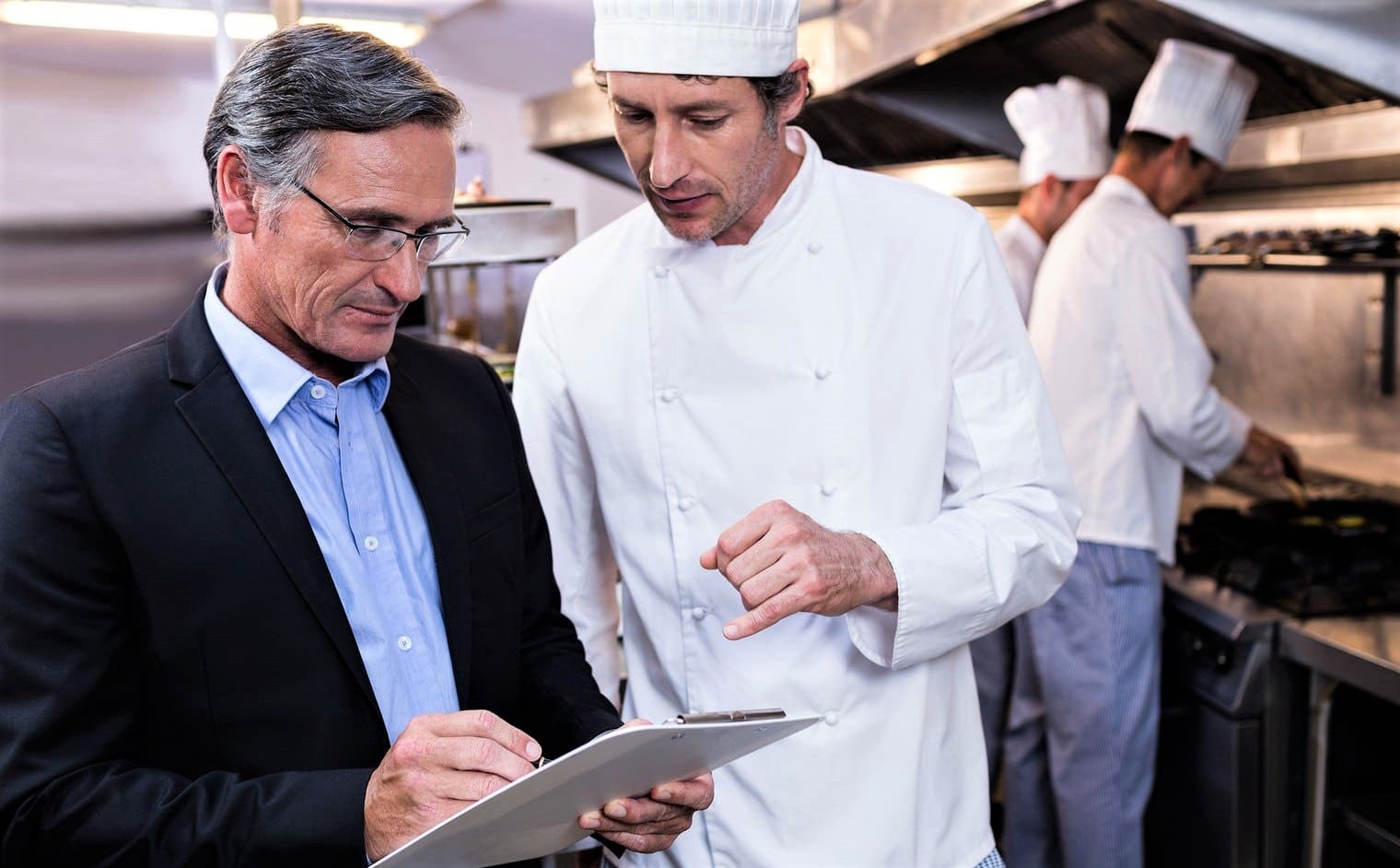 well-dressed manager in suit speaks to chef in white hat of successful restaurant