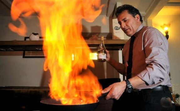 chef uses flaming pan in dynamic action shot cooking in restaurant kitchen