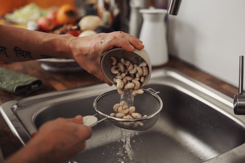 A cook rinsing cashews in a fine mesh sieve. 