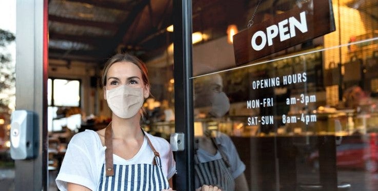 young woman in facemask stands at newly reopened restaurant during covid crisis