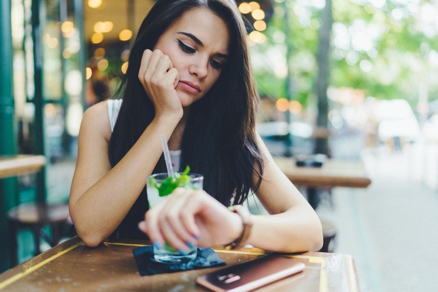 unhappy woman sitting in restaurant checks watch