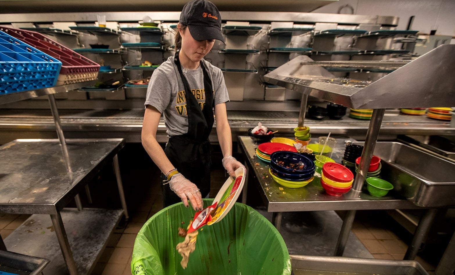 young woman scoops dead plate of food waste into restaurant bin