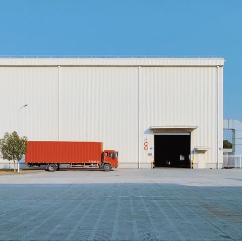 Food distributors' orange delivery trucked parked outside of a warehouse. Blue skies above.