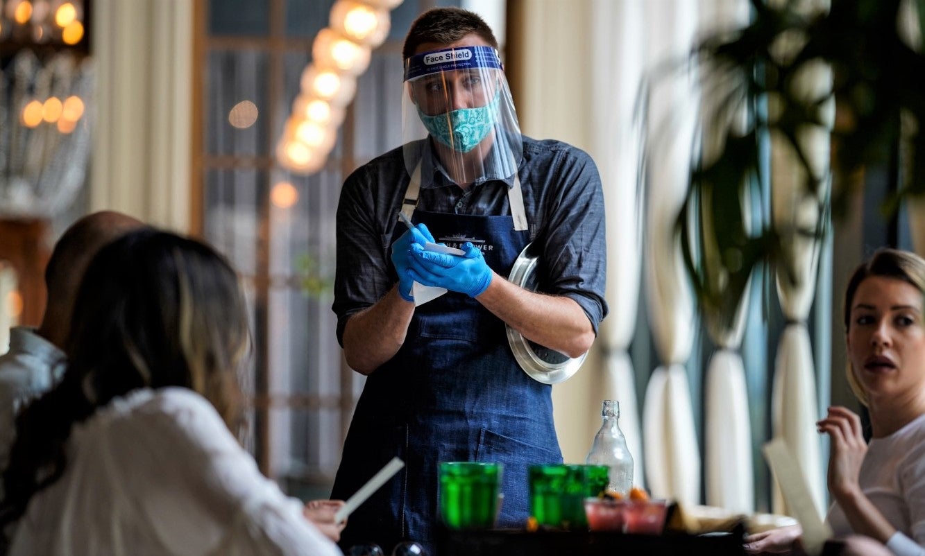 waiter in protective gear serves table of women in restaurant during covid