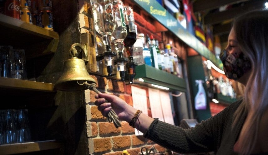 young woman behind bar rings bell for last orders in pub