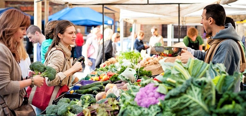 young woman purchases organic produce from man at local farmer's market