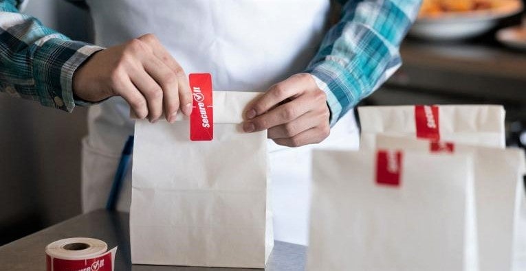 restaurant worker prepares food bags for no-contact delivery