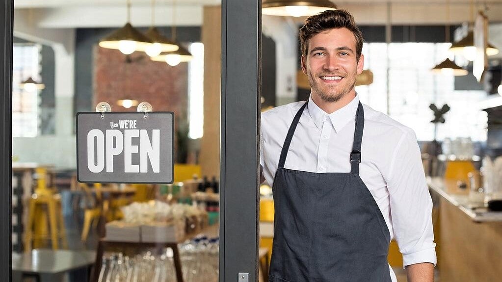 handsome young waiter in white shirt stands in newly opened restaurant