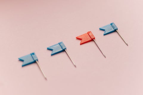 Four mini flag pins, three blue and one red, laid out on a pale pink surface