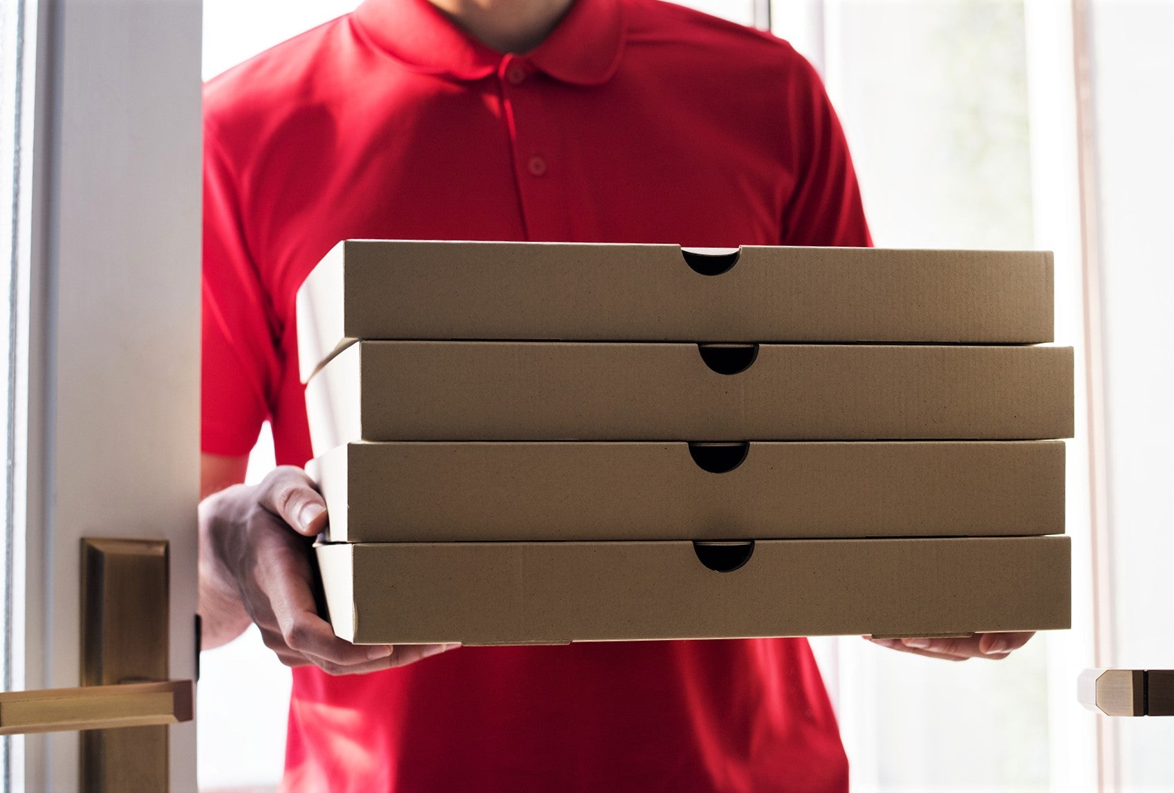 pizza delivery man in red shirt carrying stack of hot fresh pizzas
