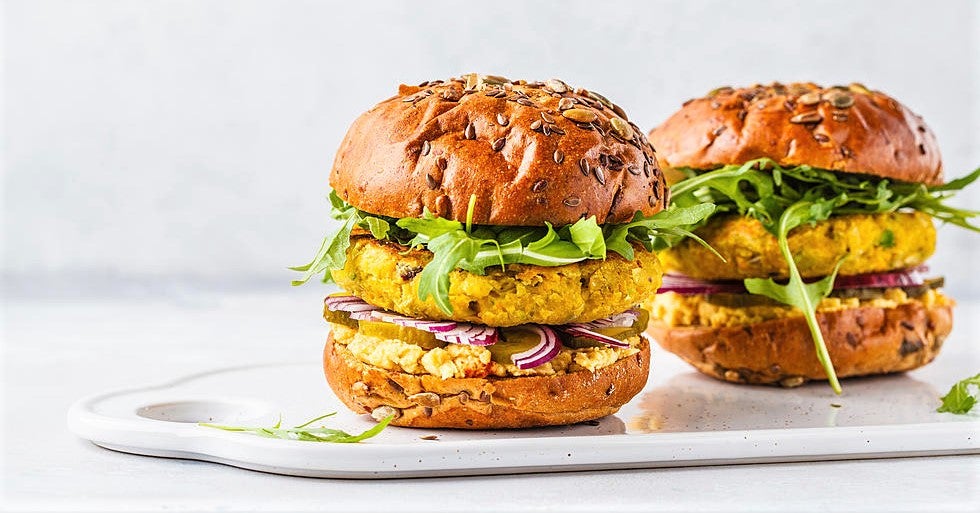 pair of plant-based meats in brown seeded bun on white ceramic serving platter