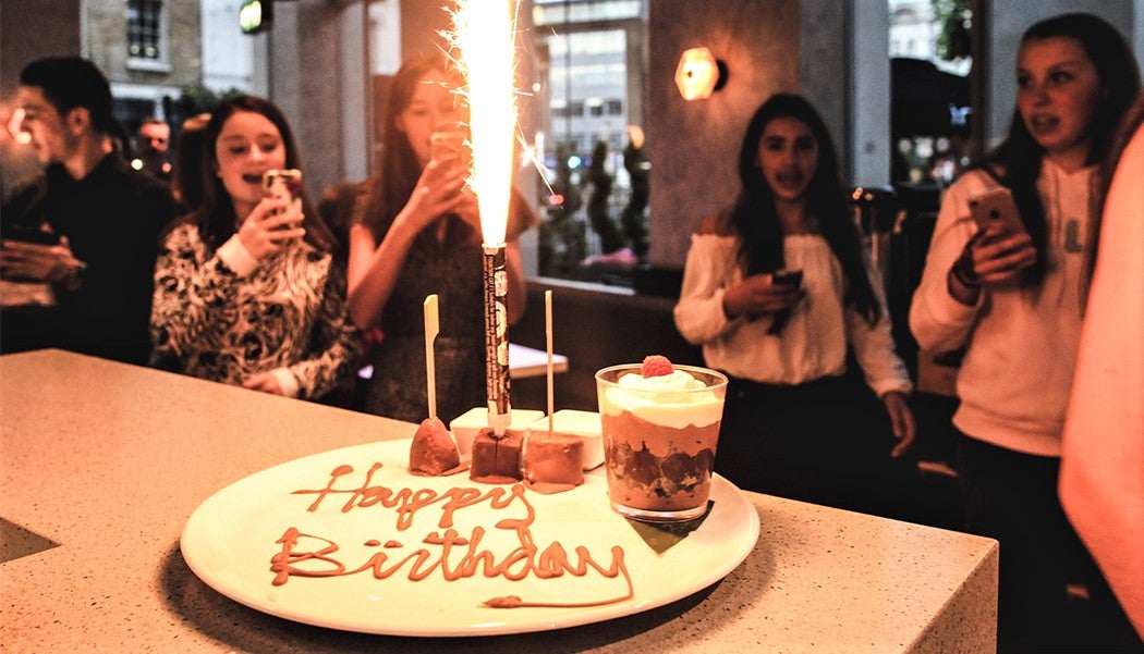 group of young women celebrate birthday party with large cake and sparkler