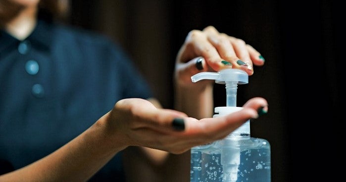 woman using bottle of hand sanitizer in restaurant
