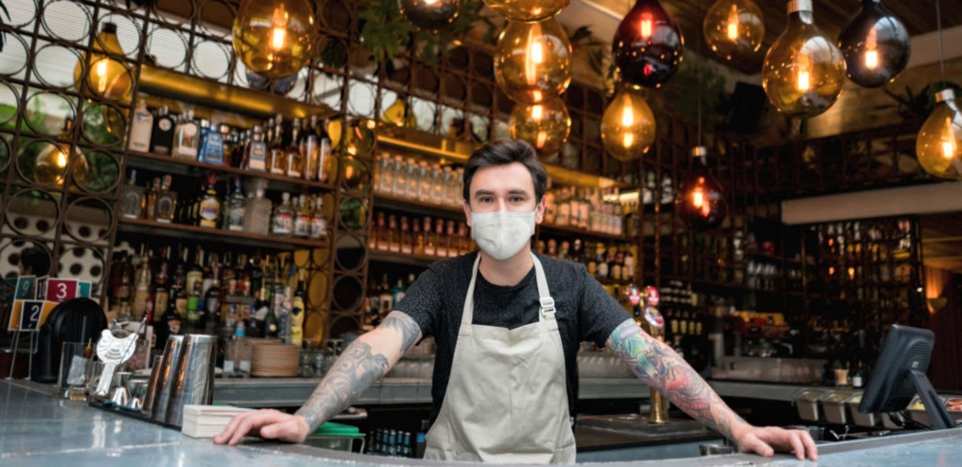 barman in face mask stands behind bar in newly reopened restaurant