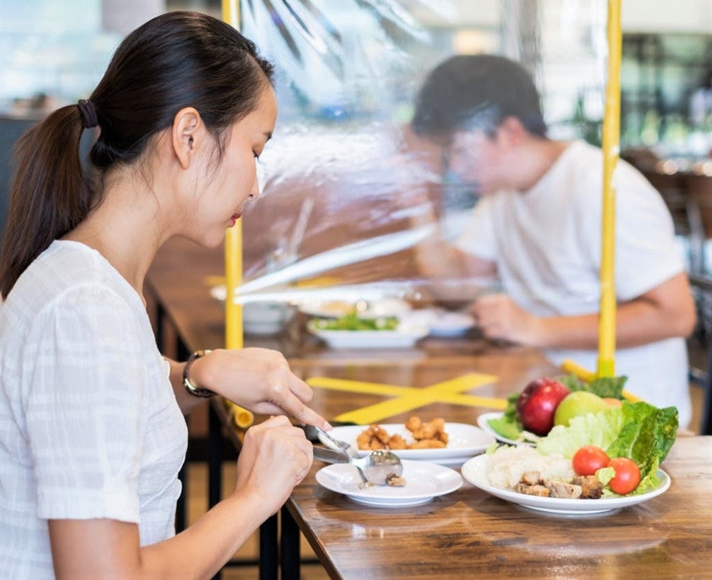 woman eats in asian restaurant with plastic barrier between her and other diner