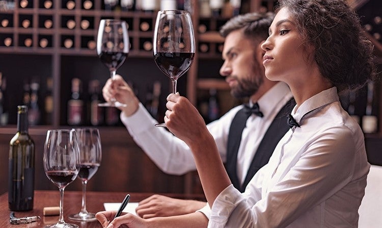 pair of wine experts examine glasses of red wine in restaurant cellar
