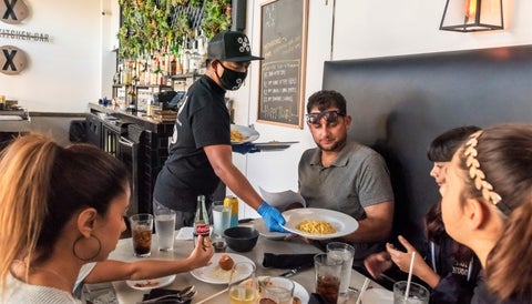 restaurant worker wearing face mask serves table of patrons