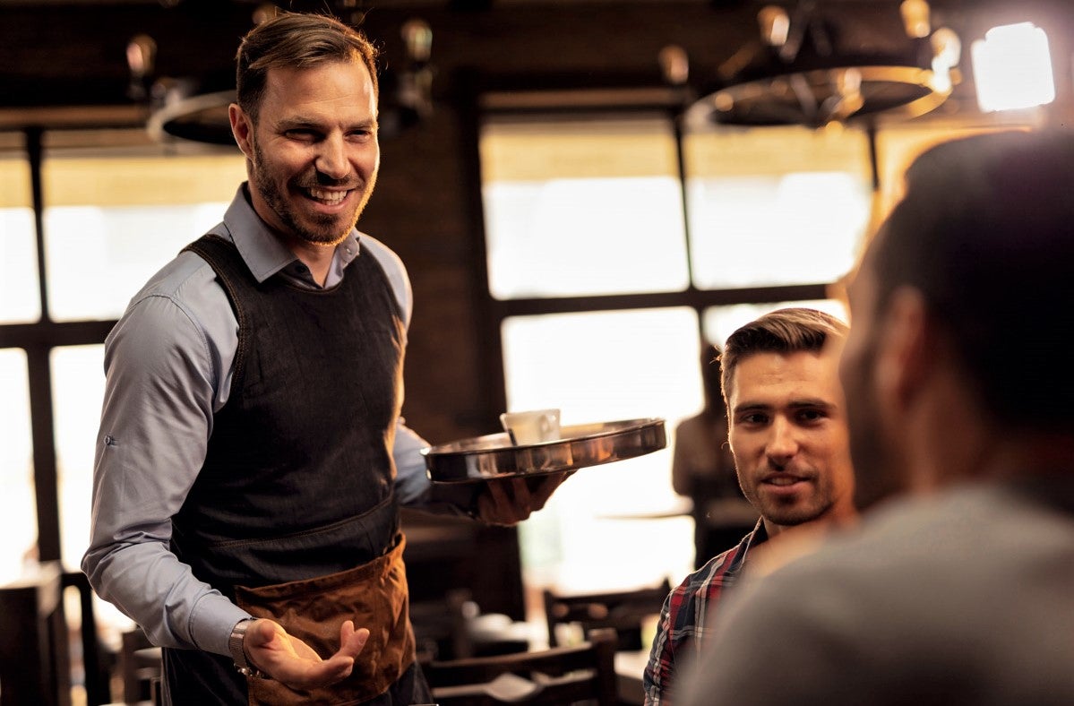 handsome male waiter in vest and button-down shirt makes recommendations to repeat customers