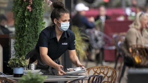 waitress in face mask clears table in outdoor patio of restaurant during covid crisis