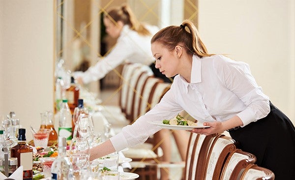 waitress in white shirt turns table in restaurant during dinner service