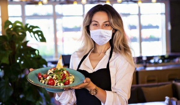waitress wearing face mask carries tray in incubator kitchen