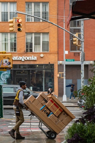 A delivery person wheels a hand truck full of packages outside. 